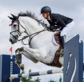 Kendal Lehari riding a grey horse over a jump in the show ring